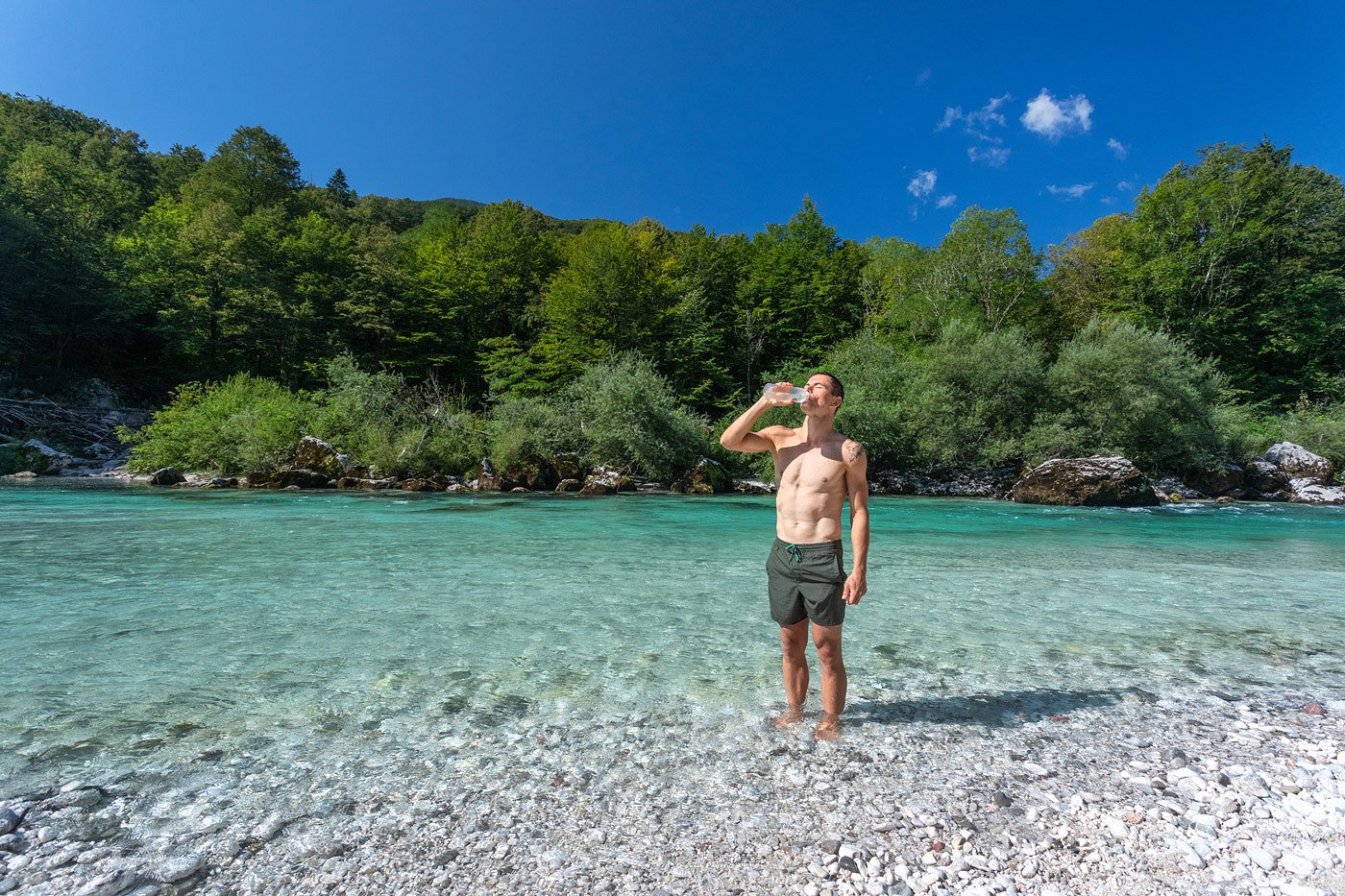 The Soča refreshes us at every step A tourist in a bathing suit stands in the Soča River and drinks water from a bottle