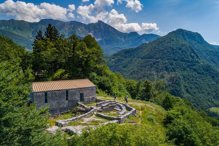 Hikers walk through the ruins, in the background Krn mountain