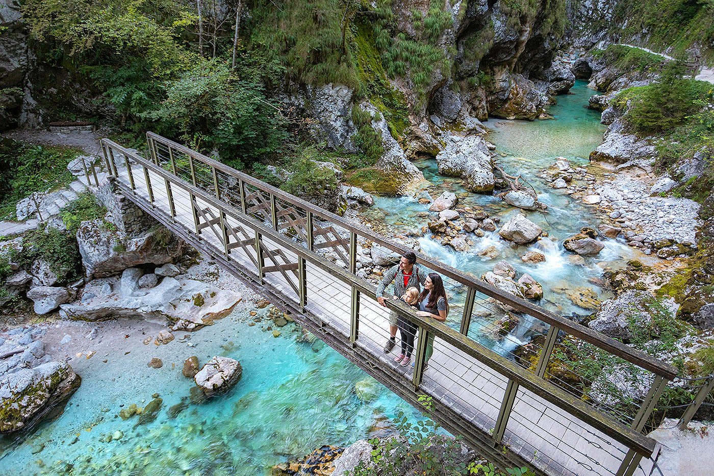 Družina uživa v razgledih na lesenem mostu, ki prečka zelenomdro Tolminko. 
